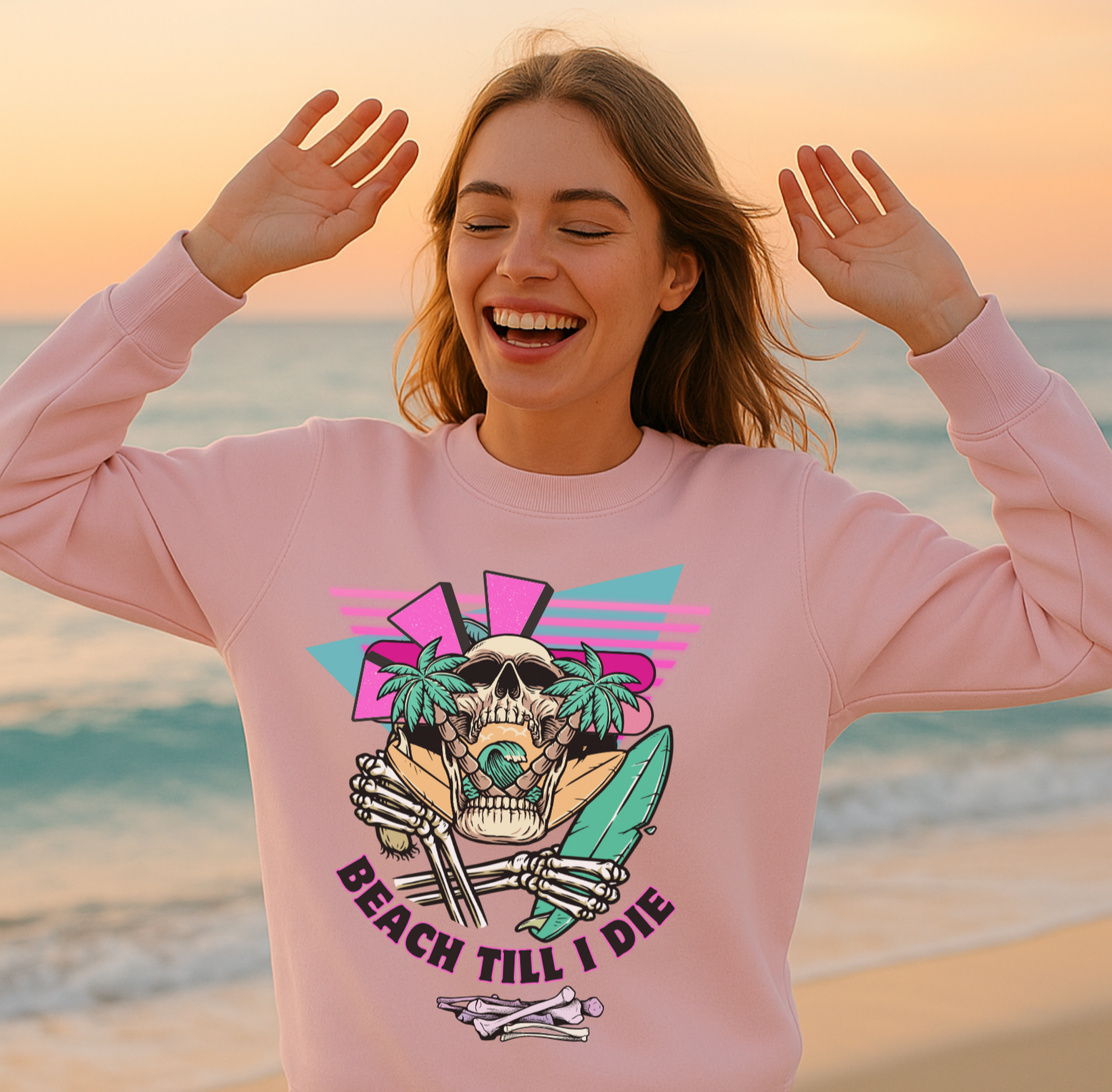 Woman wearing a pink sweatshirt with a skull design on a beach at sunset