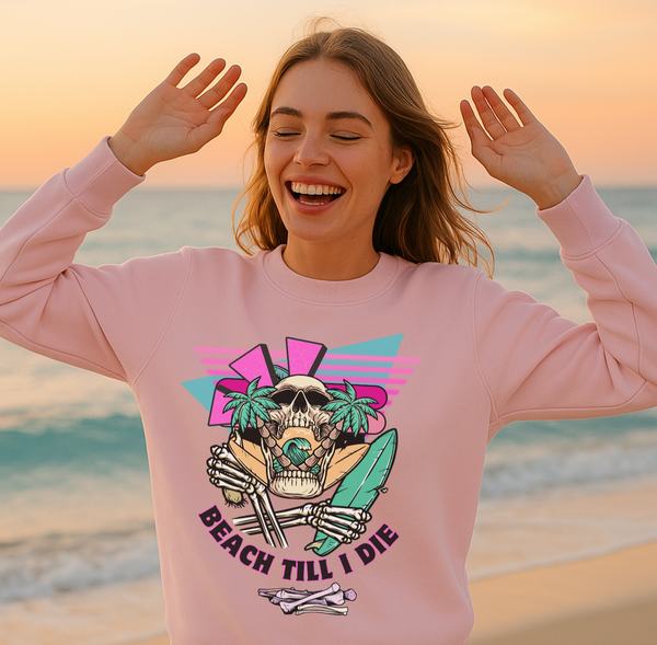 Woman wearing a pink sweatshirt with a skull design on a beach at sunset